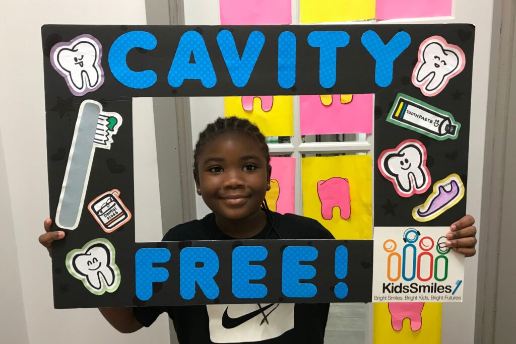 Young person holding and looking through poster frame that says "Cavity Free!"