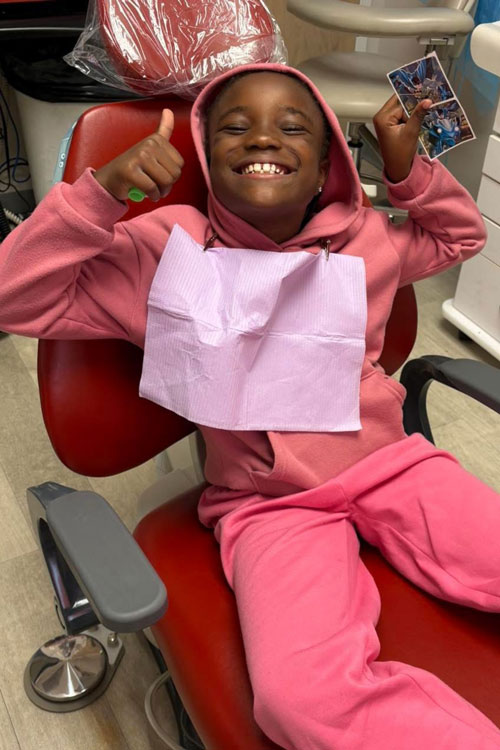 young patient in a dental chair giving two thumbs up 
