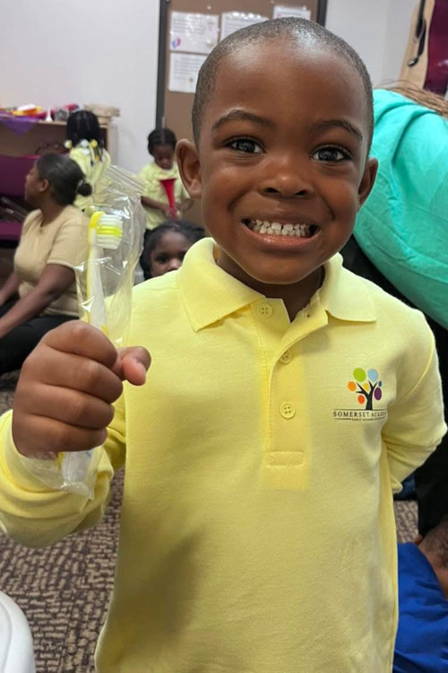 young boy smiling holding a toothbrush wrapped in celophane