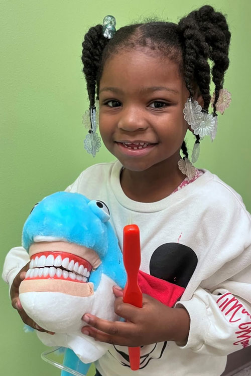young dental patient with pigtails holding a stuffed animal shark
